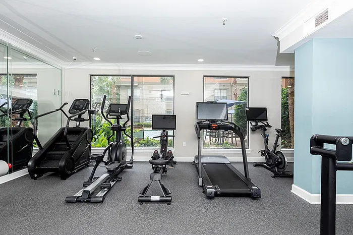 Bright and modern gym with state-of-the-art cardio equipment, including treadmill and stationary bike, overlooking lush garden views.