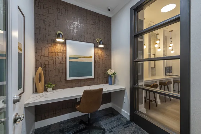 Chic corner workspace with modern decor, elegant lighting, and a large window providing a view into a stylish meeting area.