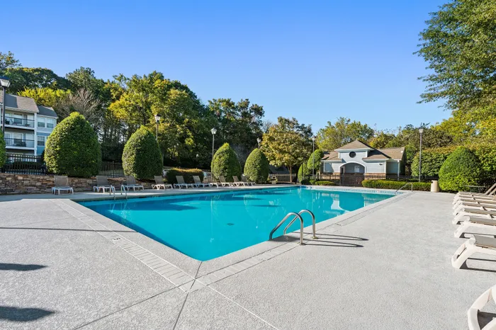 Inviting apartment complex pool surrounded by lush greenery and modern lounge chairs on a sunny day.