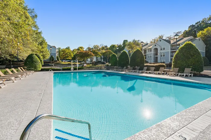 Inviting outdoor pool area with sun loungers, surrounded by lush greenery and stylish apartment buildings in the background.
