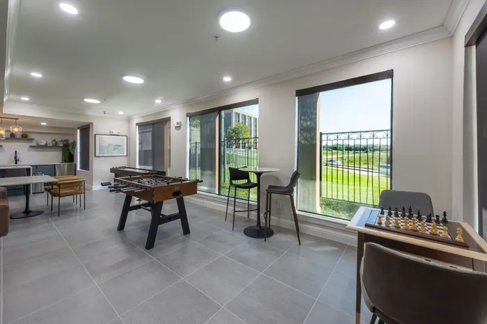 Elegant recreation room with modern lounge seating, foosball table, and vibrant street view through large windows.