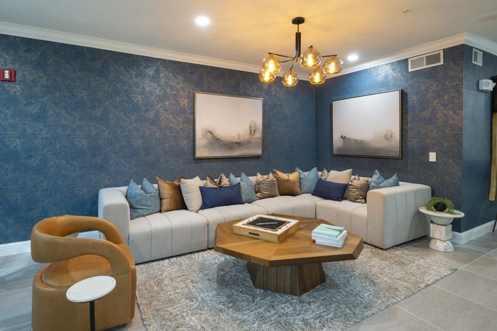 Chic living room with elegant blue wallpaper, plush sectional sofa adorned with stylish throw pillows, and a modern geometric coffee table under designer lighting.