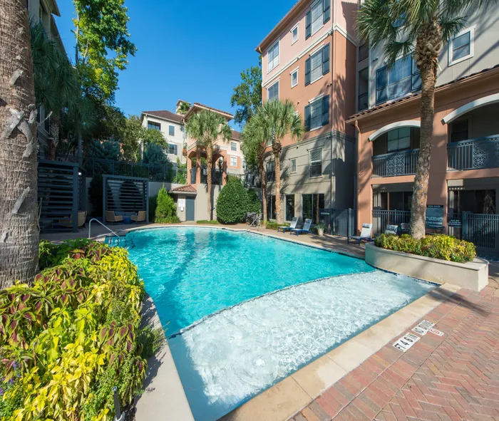Elegant apartment complex featuring a sparkling pool surrounded by lush landscaping and modern architecture.