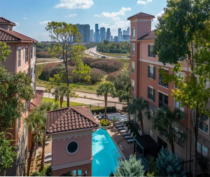 Charming urban apartment complex with a sparkling pool, lush landscaping, and stunning city skyline views.