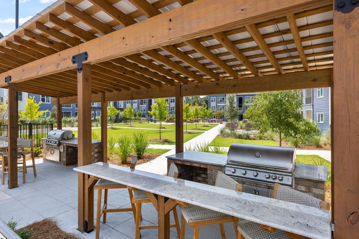 Outdoor kitchen with grills and bar seating under a pergola