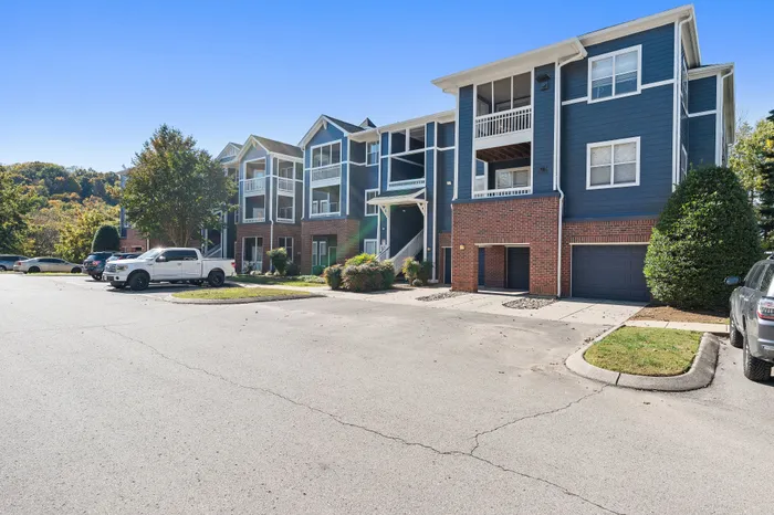 Charming and modern apartment complex with elegant brick and blue siding, surrounded by scenic greenery and ample parking space.