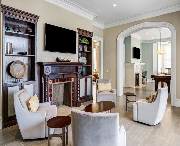 Luxurious living room featuring elegant chairs, a classic fireplace, built-in bookshelves, and seamless flow into an entertainment area with a pool table.