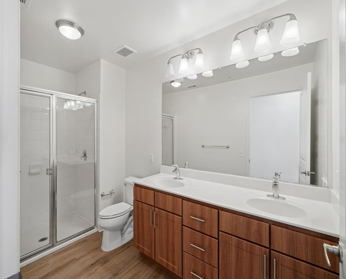 Elegant bathroom with double sinks, modern lighting, and glass-door shower featuring stylish wood cabinetry.