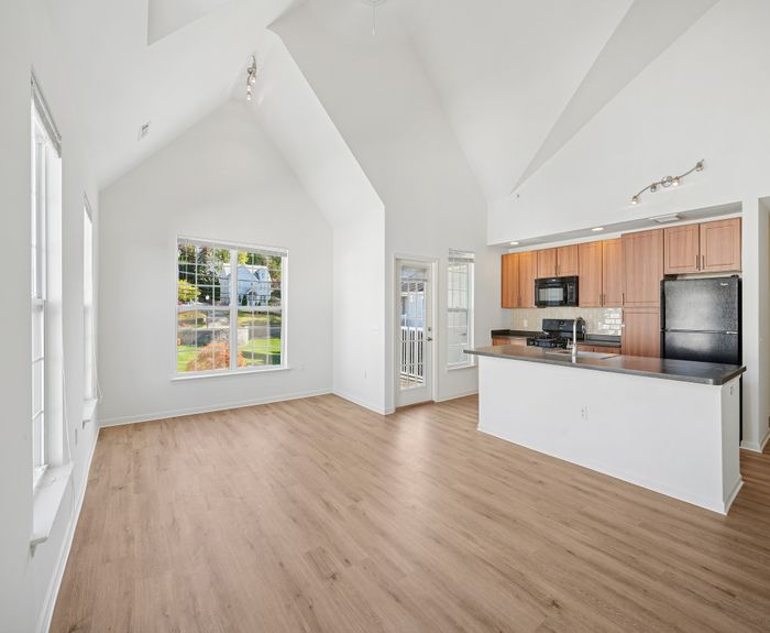 Bright and airy open-concept living space with vaulted ceilings, modern kitchen with wooden cabinetry, and sleek flooring, featuring large windows that offer scenic views.