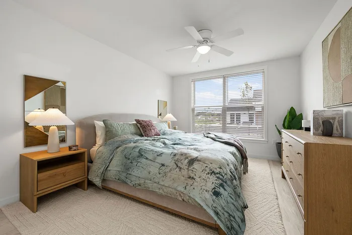 Bright and inviting bedroom with a chic design, featuring a cozy bed with stylish bedding, elegant wooden furniture, and abundant natural light through large windows.