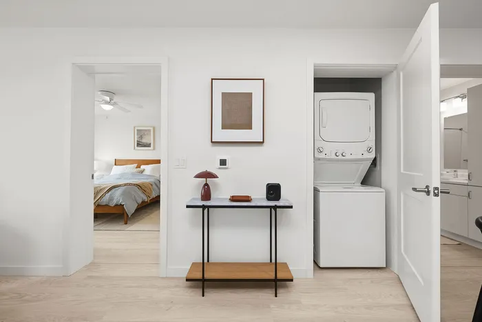 Modern apartment interior with a cozy bedroom, sleek white cabinetry, and a convenient in-unit laundry setup.