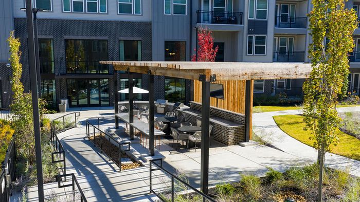 Chic outdoor lounge area with modern seating and pergola amidst lush apartment complex landscape.