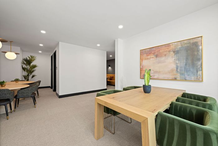 Chic work from home area with wooden table, plush green chairs, modern artwork, and cozy ambiance.