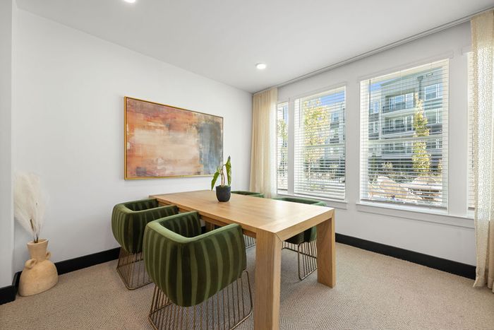 Bright co-working lounge with modern green chairs, elegant wooden table, and large windows offering scenic views.