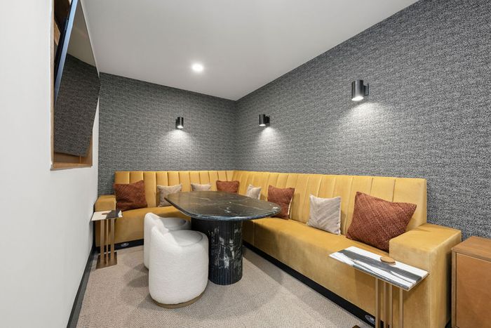 Chic and contemporary TV lounge area featuring a plush mustard sectional sofa, textured gray walls, and elegant marble-top tables, perfect for relaxation and style.