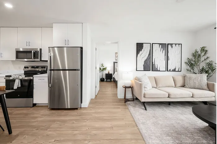 Bright and modern apartment featuring a sleek kitchen with stainless steel appliances, adjacent to a cozy living area adorned with elegant decor and a comfortable sofa.