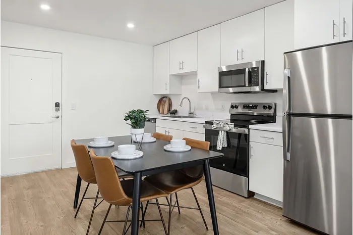 Modern kitchen and dining area featuring sleek stainless steel appliances, elegant white cabinetry, and a stylish dining table with leather chairs.