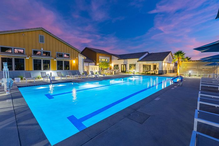 Inviting evening view of a luxurious poolside area with elegant lounge chairs and modern architecture, set against a vibrant sunset sky.