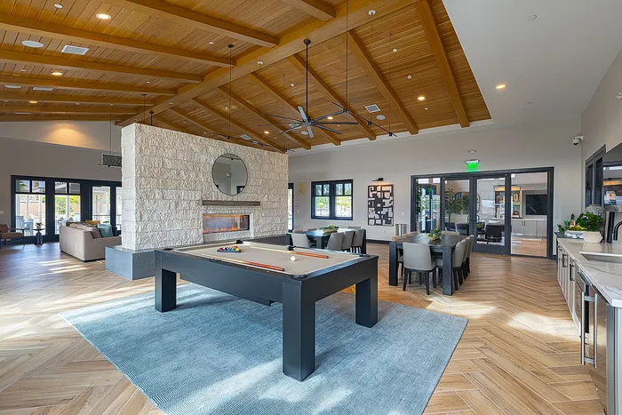 Elegant community lounge featuring a stylish billiards table, cozy fireplace, and modern dining area under stunning wood-beamed ceilings.