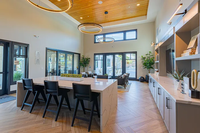 Modern communal space with high ceilings, elegant lighting, and stylish decor including a central seating area and sleek wooden flooring.