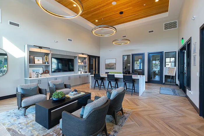 Elegant community lounge featuring modern seating, stylish decor, and a sleek entertainment area with a wooden ceiling and vibrant lighting accents.