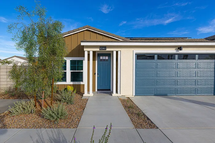 Charming single-story home with a stylish facade, featuring a welcoming blue door and a spacious double garage, beautifully landscaped with modern greenery and clean pathways.