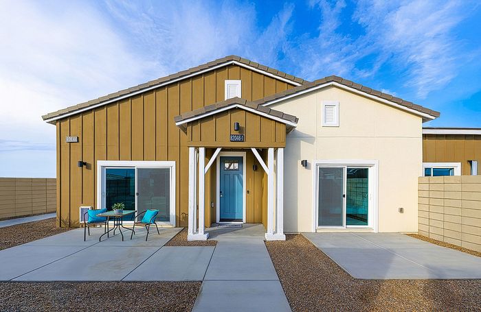 Charming modern home with a bright blue front door, stylish patio seating, and clean architectural lines under a clear blue sky.