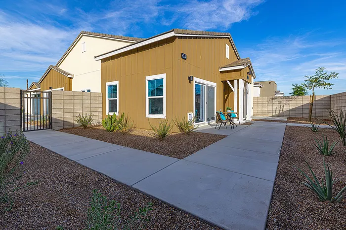Contemporary desert-style home with a charming facade, inviting patio seating, and vibrant landscaping under a clear blue sky.
