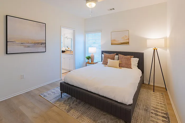 Elegant bedroom featuring cozy bed with decorative pillows, stylish floor lamp, and serene art, offering a modern retreat with en-suite bathroom.