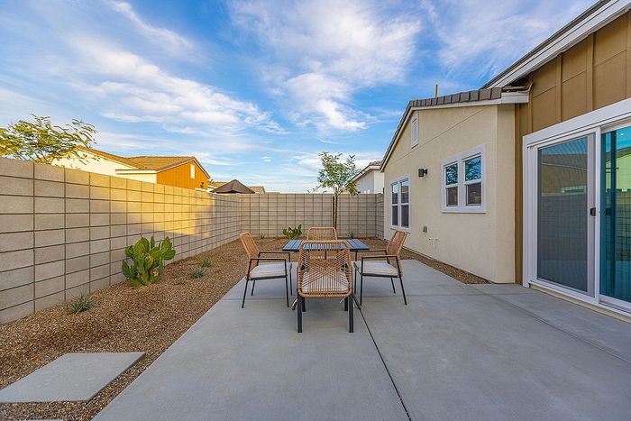 Inviting outdoor patio with sleek seating set, surrounded by a modern privacy wall and vibrant desert landscaping, under a clear blue sky.