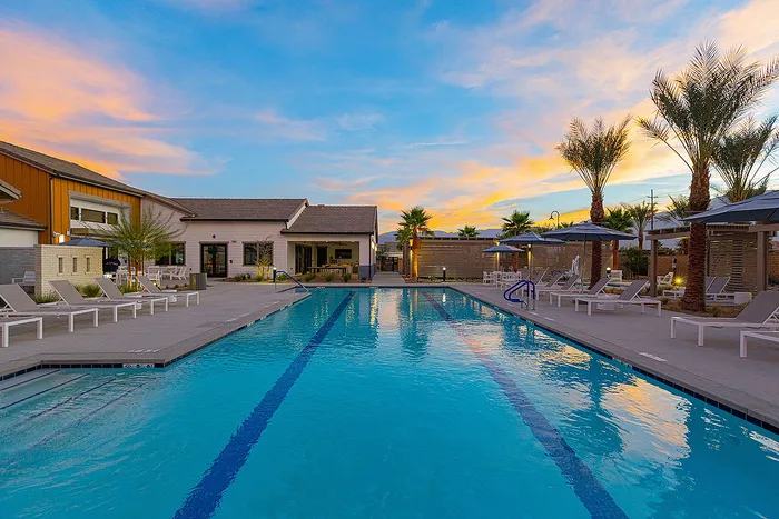 Luxurious apartment pool area with modern lounge chairs and tall palms, set against a stunning sunset backdrop.