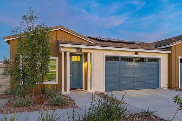 Charming modern home with a welcoming blue door, stylish garage, and appealing desert landscaping, set against a vibrant evening sky.
