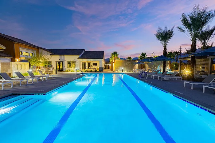 Luxurious resort-style swimming pool area at sunset, featuring comfortable lounge chairs and tropical palm trees, perfect for relaxation and enjoyment.
