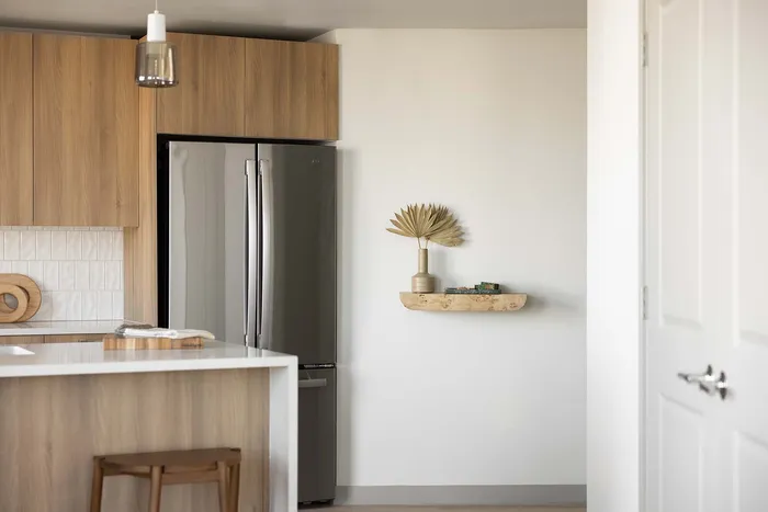Modern kitchen with sleek wooden cabinets, stainless steel fridge, minimalist decor on a floating shelf, and a stylish island with bar stool seating.