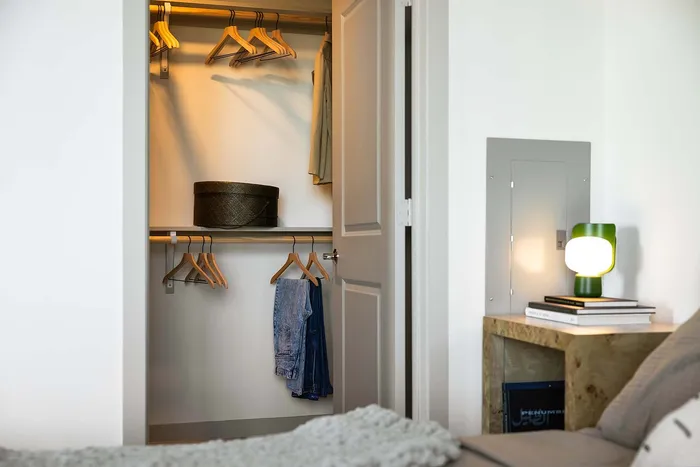 Modern bedroom with a neatly organized walk-in closet, featuring stylish wood hangers and cozy lighting beside a sleek nightstand with a trendy lamp.