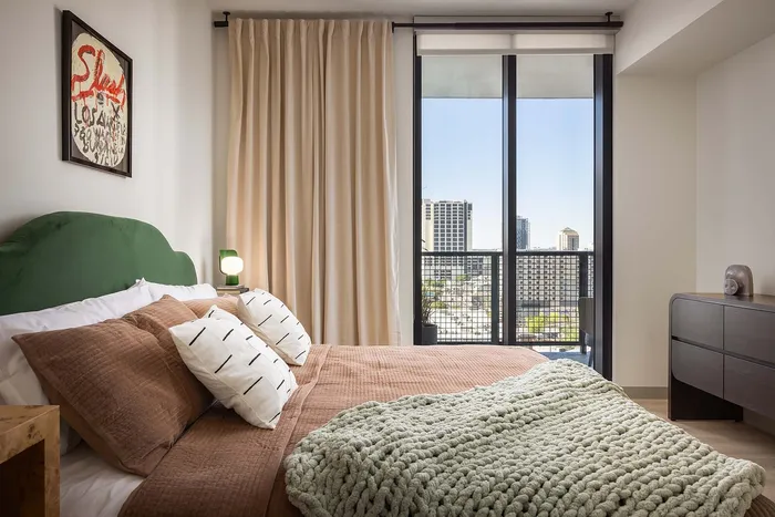 Modern bedroom with cozy decor, featuring a plush bed, stylish art, and a stunning city view through floor-to-ceiling windows.