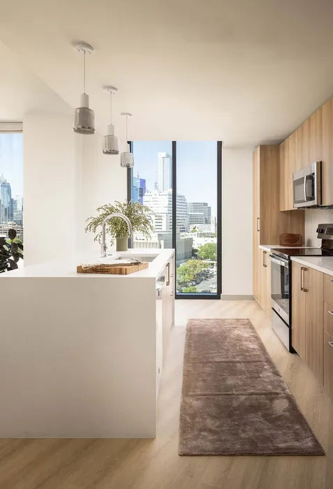 Modern kitchen with sleek wooden cabinets, stylish island, and panoramic city views through large windows.