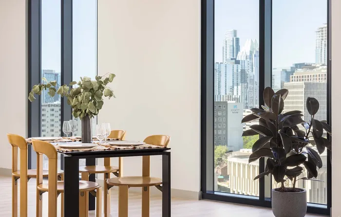 Contemporary dining area with chic wooden chairs, stylish table set, and expansive cityscape views through large windows.
