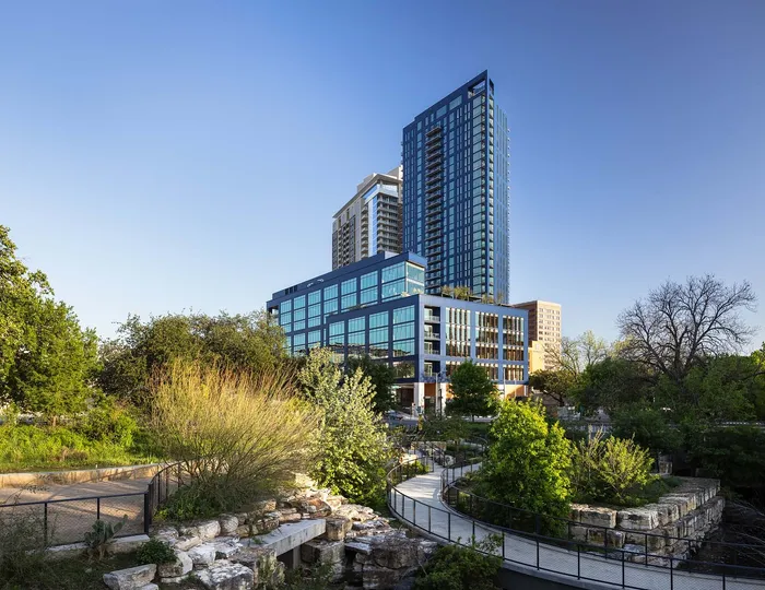 Stunning urban high-rise surrounded by lush greenery, featuring modern architecture and expansive glass windows.