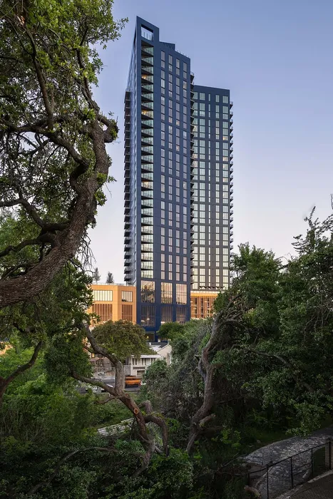 Elegant high-rise residential tower with sleek glass facade, nestled amidst lush greenery offering serene and modern urban living.