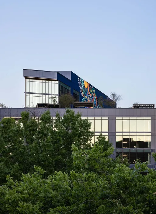 Modern architectural building with large glass windows and vibrant mural, surrounded by lush greenery.