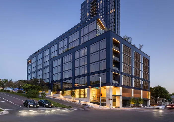 Modern luxury apartment building with expansive glass windows and elegant lighting at dusk, located on a vibrant street corner.