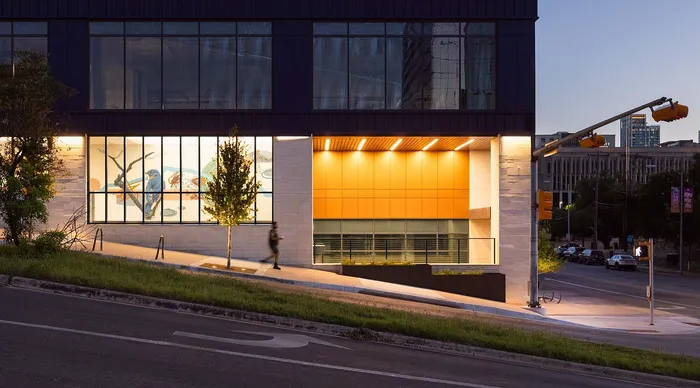 Modern urban building with large windows and vibrant exterior lighting, located on a well-lit street corner.