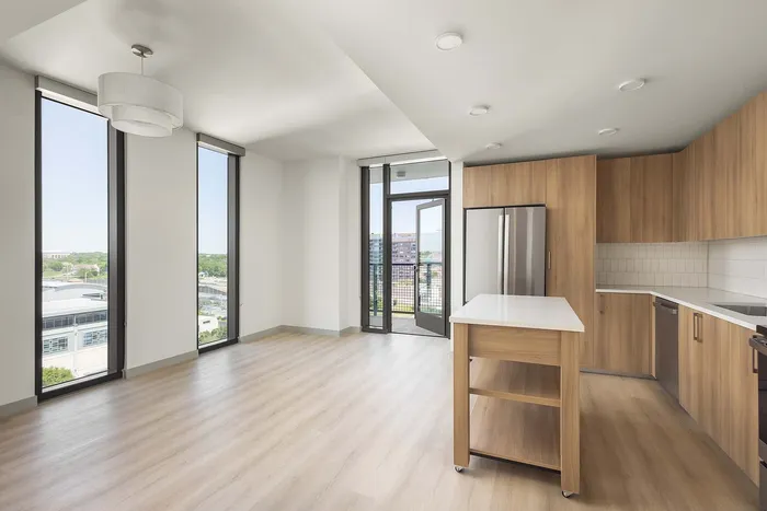 Sleek and modern apartment featuring a bright open kitchen with stainless steel appliances, elegant wooden cabinetry, and expansive windows offering stunning city views.