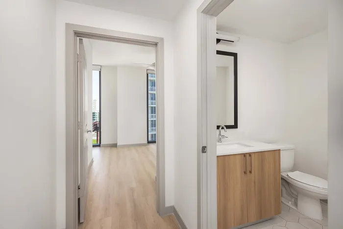 Bright, modern apartment hallway with sleek wood flooring and a stylish bathroom featuring contemporary fixtures.