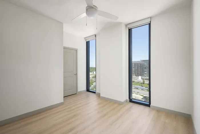 Bright and modern apartment interior featuring elegant hardwood floors, tall windows with city views, and a ceiling fan for comfort.