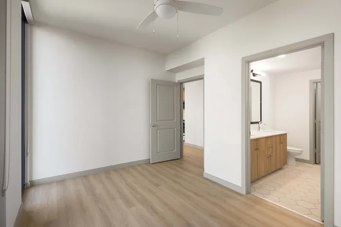 Bright, modern apartment room with sleek hardwood floors, white walls, and an en-suite bathroom featuring a stylish vanity and elegant tile flooring.