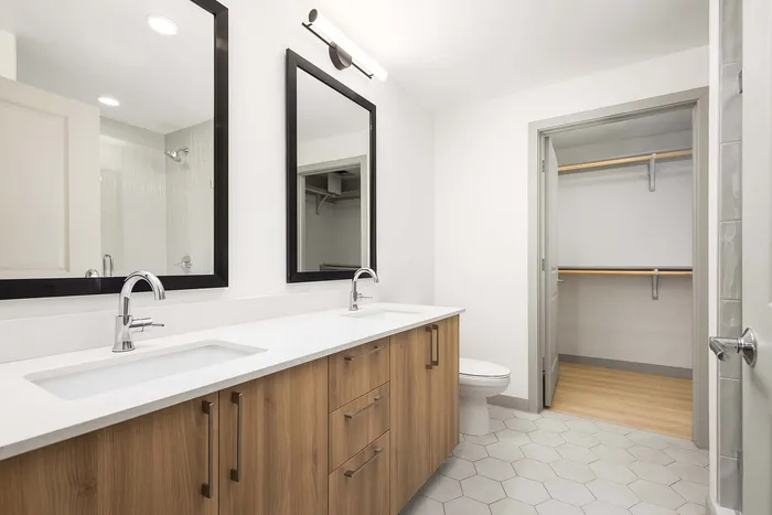 Contemporary bathroom with dual sinks, stylish wood cabinetry, and spacious walk-in closet, perfect for modern living.