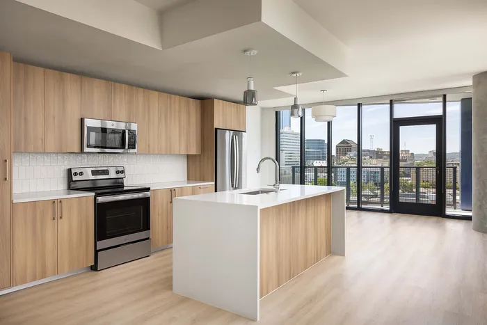 Modern kitchen with sleek wooden cabinetry, stainless steel appliances, and a spacious island, overlooking a panoramic city view through large windows.