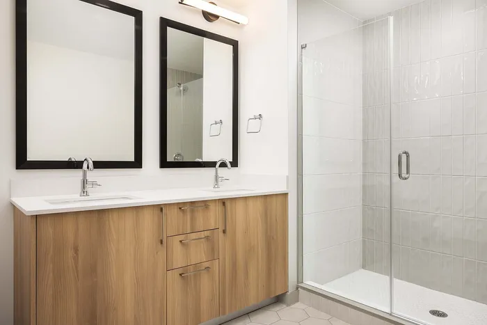Elegant bathroom with dual sinks, modern mirrors, wood cabinetry, and a sleek glass shower.